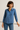 Woman wearing a blue patterned shirt and jeans on a plain background