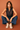 Woman sitting on the floor wearing a black sleeveless top and blue pants against a brown background