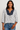 Woman wearing a white blouse with blue floral patterns and blue jeans on a plain background