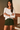 Woman wearing a white top and green skirt standing indoors.