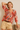 Woman wearing a colorful blouse with abstract patterns and beige shorts against a plain background