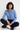 Woman wearing a blue shirt and black pants sitting on a white floor.
