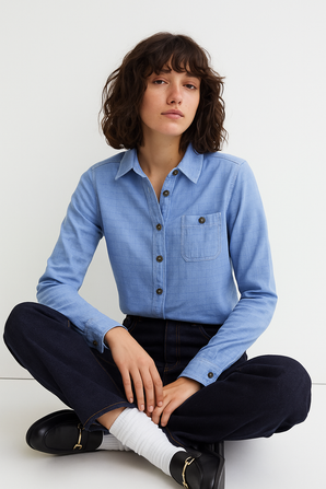 Woman wearing a blue shirt and black pants sitting on a white floor.
