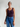 Woman wearing a dark purple tank top and blue jeans against a plain background