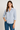 Woman wearing a light blue shirt and blue jeans against a plain background