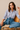 Woman wearing a checkered shirt and jeans sitting on a chair.