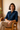 Woman wearing a blue shirt sitting on a wooden chair with a neutral background