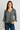 Woman wearing a black and gray patterned blouse with blue jeans on a gray background