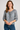 Woman wearing a patterned blouse and blue jeans on a plain background