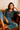 Woman sitting on a couch wearing a patterned top and jeans.