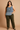 Woman wearing a patterned top and olive green pants on a beige background