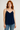 Woman wearing a navy blue spaghetti strap top and blue jeans on a plain background