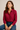 Woman wearing a red patterned shirt and blue jeans against a beige background