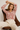 Woman sitting on a brown leather chair wearing a red and white patterned shirt and beige pants.