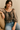 Woman wearing a sheer blouse with long sleeves and blue jeans sitting on a beige couch.