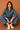 Woman wearing a blue patterned shirt and blue pants sitting on the floor against a brown background