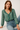 Woman wearing a green patterned top and blue jeans against a white background