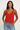 Woman wearing a red tank top and blue jeans against a plain background