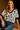 Woman wearing a black and white floral top with blue jeans on a brown background