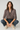 Woman wearing a patterned blouse and jeans sitting on the floor against a plain background