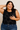 Woman wearing a black floral sleeveless top and blue jeans against a beige background