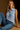 Woman wearing a light blue sleeveless shirt and jeans against a brown background