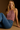 Woman wearing a pink top and blue jeans sitting on a brown background