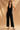 Woman wearing a black sleeveless top and wide-leg pants against a beige background