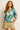 Woman wearing a tropical leaf patterned top with a beige skirt on a plain background