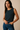 Woman wearing a sleeveless checkered top and blue jeans against a beige background